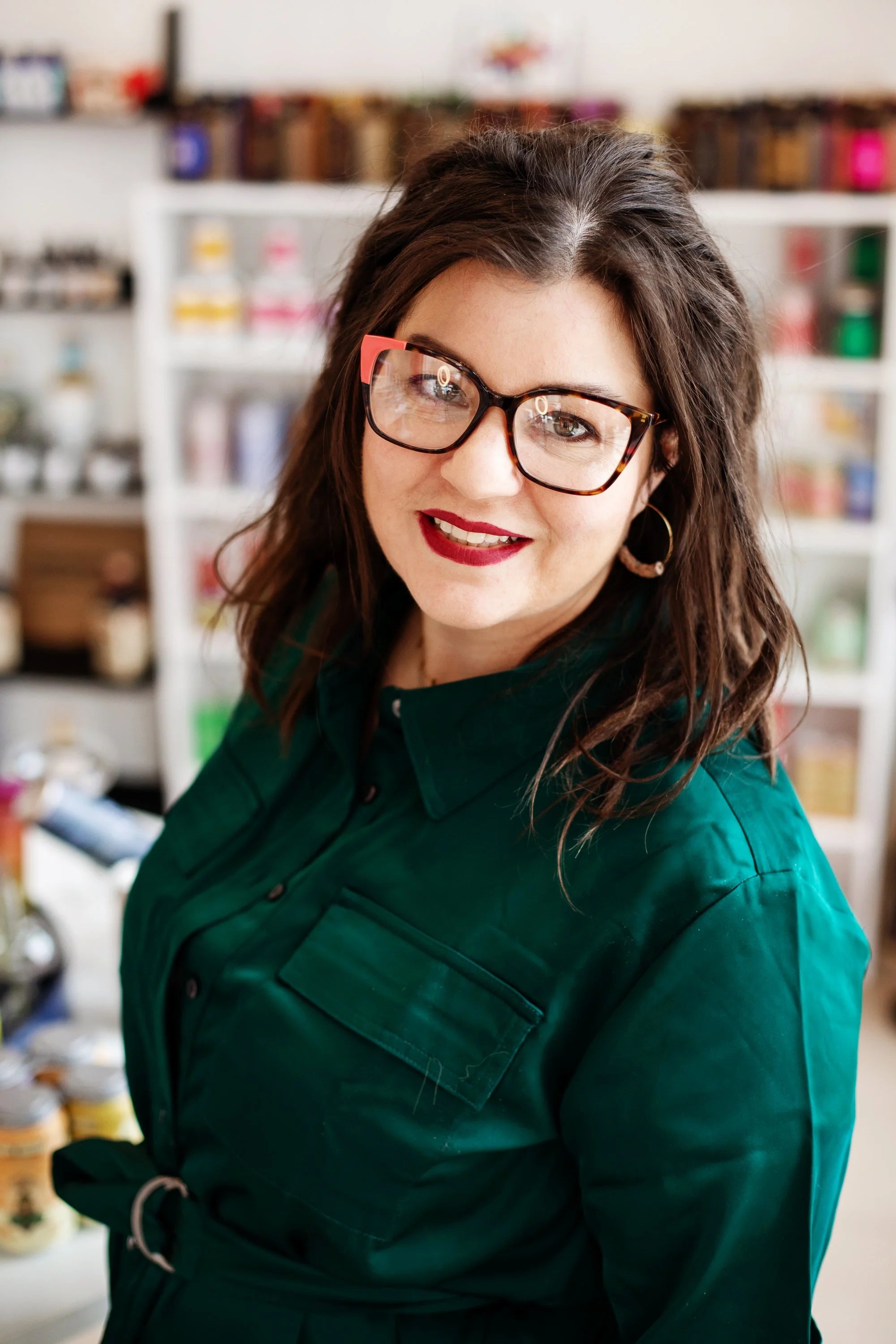 Beyond Bottleshop's owner smiling in a cream blazer inside the shop, colorful bottles on the shelves behind her