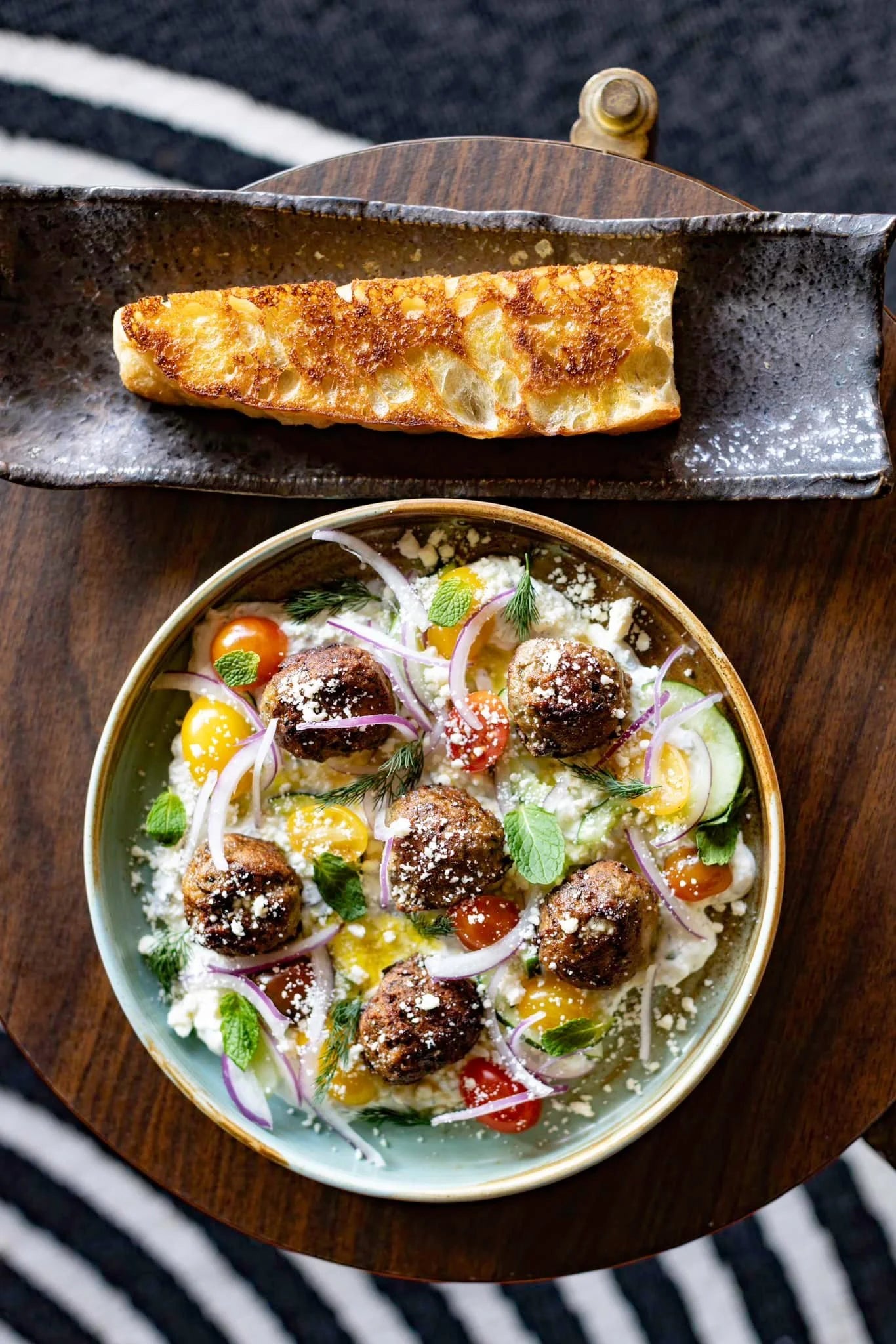 A Mediterranean meatball bowl with cherry tomatoes, red onion, herbs and crumbled cheese, served with grilled bread