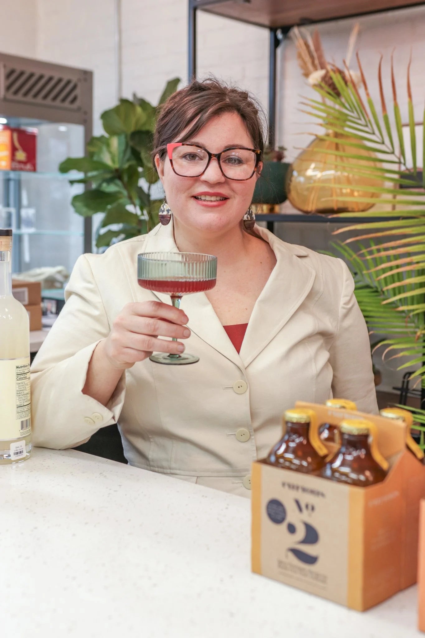 Beyond Bottleshop's owner raising a coupe of a pink non-alcoholic cocktail behind the shop counter